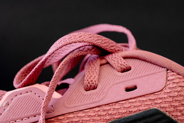 Extreme close up of a a pink shoe with pink shoelaces against a black background.