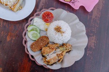 A delicious plate of Ayam Geprek with white rice, spicy chili sauce, and fresh vegetables, a classic Indonesian meal perfect for food and travel themes