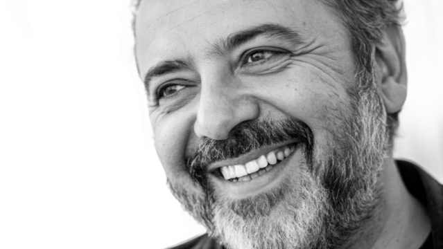 Close up black and white shot of a smiling man with a beard looking to the side of the frame
