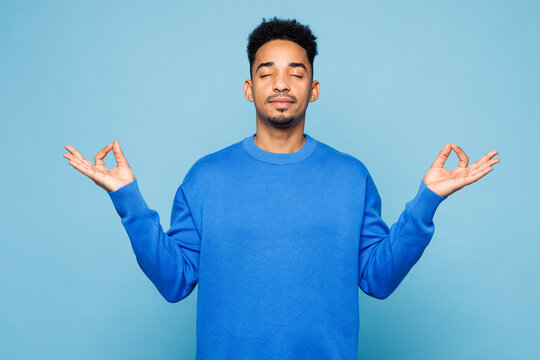 Young man wear sweatshirt casual clothes hold spreading hands in yoga om aum gesture relax meditate try to calm down isolated on plain pastel light blue background studio portrait. Lifestyle concept.