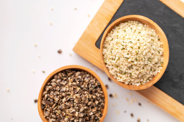 Cleaned and whole hemp seeds in wooden bowls, kitchen writing board on gray background. Superfood, natural organic seeds for healthy eating, source of protein, vitamins and omega 3. Healthy food 