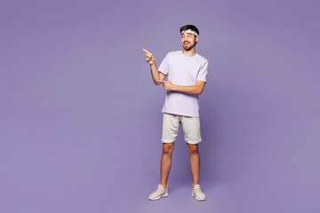 Full body young strong fitness trainer instructor man sportsman wear sportswear train in home gym point index finger aside on area isolated on plain purple background. Workout sport fit abs concept. © ViDi Studio