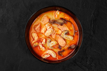 Tom yam soup with salmon, shrimp, and mushrooms in black bowl