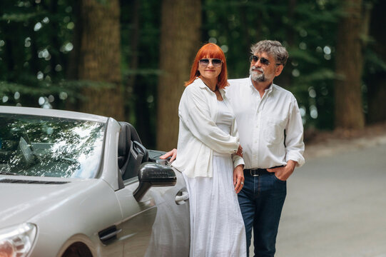 Lovely senior couple standing on the road near convertible cabriolet car
