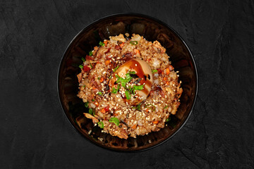 Delicious fried rice dish with egg and sesame seeds in black bowl