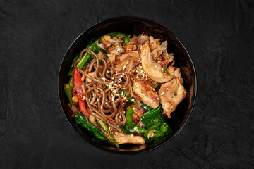 Soba noodles with chicken and vegetables filling a black bowl