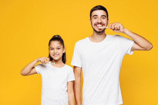 Young happy smiling parent man have fun with child girl wear casual blue pyjamas clothes. Daddy little kid daughter brushing teeth isolated on plain yellow background Father's Day Love family concept.