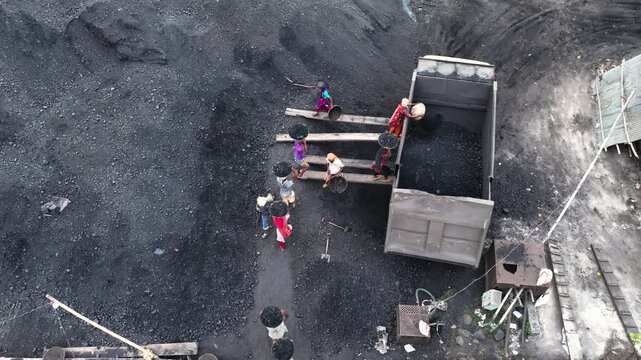 Dhaka, Bangladesh - 24 August 2025: Aerial view of laborers carrying coal in head baskets and loading a truck, contrasting with the dark coal dust.
