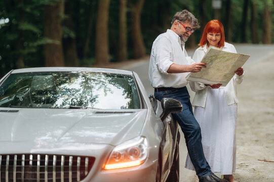 Reading the map. Lovely senior couple standing on the road near convertible cabriolet car