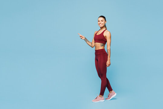 Full body young fitness trainer instructor sporty woman sportsman in red sportswear train in home gym point index finger aside on area isolated on plain blue background Workout sport fit abs concept - Powered by Adobe