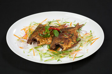 Crispy Fried Pomfret Fish with vegetable salad in plate isolated on dark background side view of Delicious Indian Seafood Dish