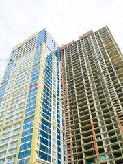 Fototapeta premium Beige-framed glass tower stands beside exposed concrete floors of unfinished building still skeletal, illustrating architectural progress and city expansion under partly cloudy sky in Danang