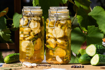 Homemade dill pickles in jars with garlic, salt, spices on wooden cutting board on an outside garden table.