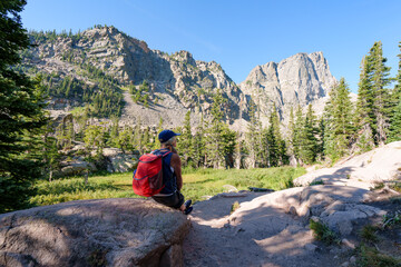 Woman hiker sitting on rock and viewing the mountains; hiking in the Colorado Rocky Mountains.