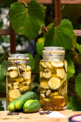 Dill pickles in a glass jar on a table in an outdoor garden. Vertical shot.
