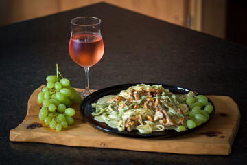 ready to eat - tagliatelle with chanterelles and grapes, served on a black plate on a wood board