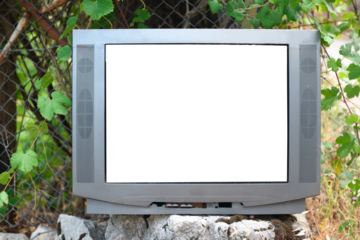 An old television with an isolated white screen abandoned in nature near a wire fence during the day.