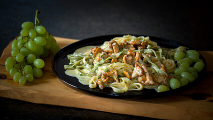 ready to eat - tagliatelle with chanterelles and grapes, served on a black plate on a wood board