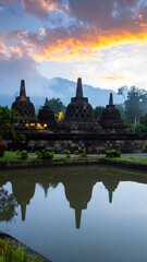 Obraz premium Stone stupas reflected in tranquil water at dawn, bathed in the warm hues of sunrise.