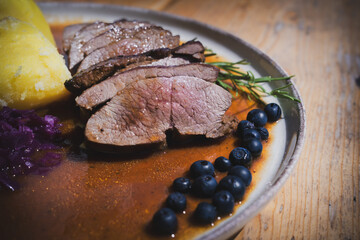 ready to eat - roasted venison from the chamois with potaoes, cabbage, braun sauce and decorated with blueberries and rosemary, served on a plate on the wood table