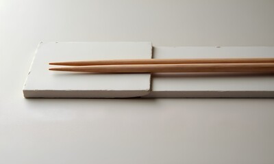 A pair of wooden chopsticks resting on a minimalist white stone holder, set against a clean, neutral beige background. A concept of zen, simplicity, and Asian cuisine.