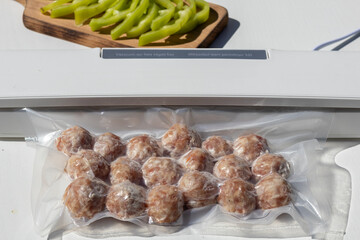 Vacuum-sealed meatballs in plastic packaging with fresh green peppers on a wooden cutting board. Ideal for meal prep and food storage.