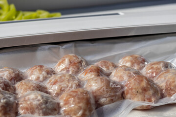 Vacuum-sealed meatballs arranged neatly in a package. Fresh ingredients are visible in the background, suggesting meal preparation.