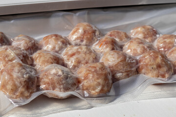 Raw meatballs packaged in vacuum-sealed plastic. The meatballs are round and have a light pink color, ready for cooking or freezing.