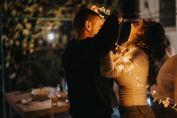A couple joyfully entangled in decorative string lights, sharing a tender moment together in the...