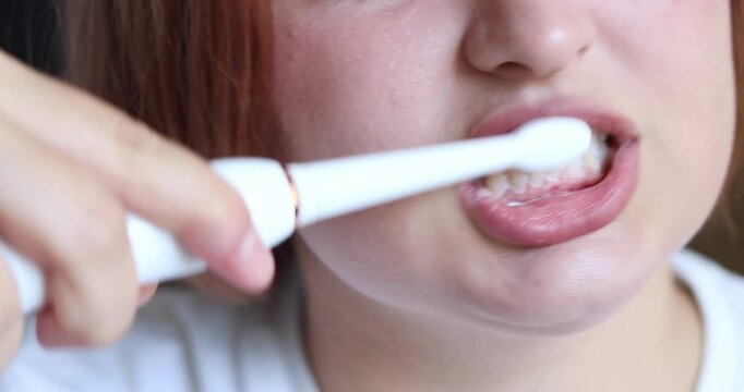 Close-up front view unrecognizable caucasian woman brushing teeth with toothbrush. Mouth of young confident lady doing morning routine in bathroom at home indoors. Dental health advertisement
