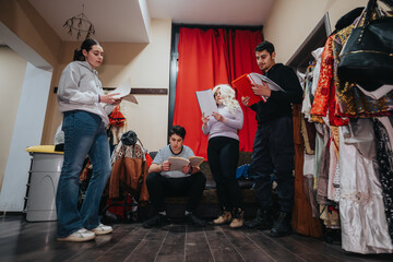 A group of actors backstage engaged in a script reading and rehearsal preparation, with colorful costumes enhancing the scene.