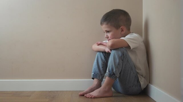 Boy sitting on the floor. A boy is kicking a child in the corner. A young boy upset by violence against his father. A boy is lifestyle seated on the ground.