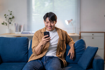 Happy asian man using smartphone while relaxing on sofa at home
