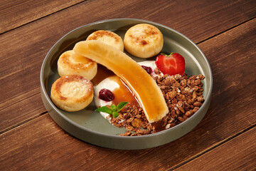 Cheesecakes with caramel sauce, banana, granola, strawberry and yogurt on wooden table