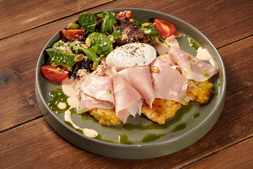 Potato pancakes with ham, poached egg and salad on wooden table