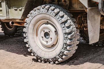 Large off road tire of a military truck parked on sand, close up view emphasizing the ruggedness and capability of the vehicle © EdNurg