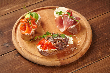 Delicious bruschetta with salmon, prosciutto, and roast beef resting on wooden board