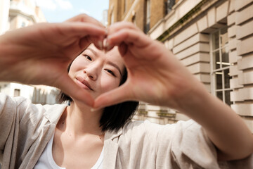 Young woman making heart shape with hands in city
