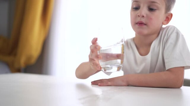 Young boy holding glass of water. Young boy drinks water from glass. A child is drinking a glass of water. A little boy with a glass lifestyle of water.