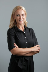 Portrait of a happy business woman with arm crossed isolated on grey background, looking at the camera and smiling.