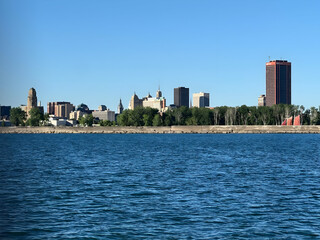 Obraz premium Expansive city skyline across a calm blue body of water under a clear sky