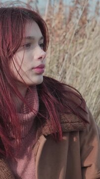 Teenage girl in side profile, looking thoughtfully into the distance, with wind blowing her hair, wearing warm autumn or winter clothing