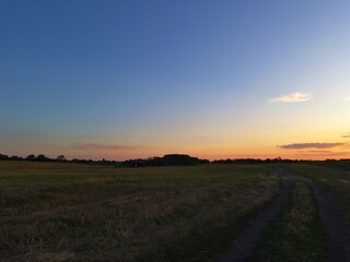 Empty dirt track leading through countryside at twilight. Rich sky tones without the sun in view.