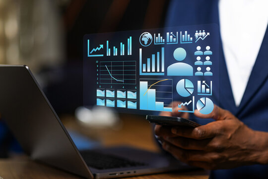 African Businessman interacts with holographic business data projected from his phone displaying glowing data visualizations, charts, and icons, analytics and technology.