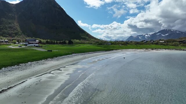 Hov beach in Gimsoy, Lofoten, with sand, waves, green meadows, farm and Hoven mountain in summer light