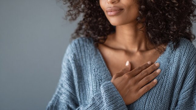A serene portrait showcases a woman in a blue sweater, hand gently placed over her heart, evoking feelings of self-love, gratitude, and inner peace. - Powered by Adobe