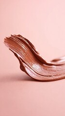 Smooth, creamy texture of brown cosmetic product swirled elegantly on a soft pink background, showcasing beauty and artistry in makeup application and design