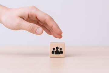 Hand hovering over a wooden cube with a group icon, illustrating teamwork and collaboration