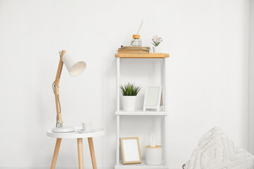 Desk lamp on small table and shelving unit with decor near white wall