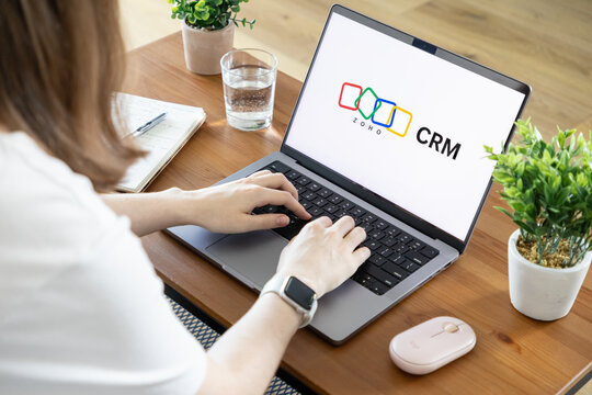 Poznan, Poland - August 23, 2025: Woman uses laptop with Zoho CRM software, managing client relationships and optimizing crucial business functions